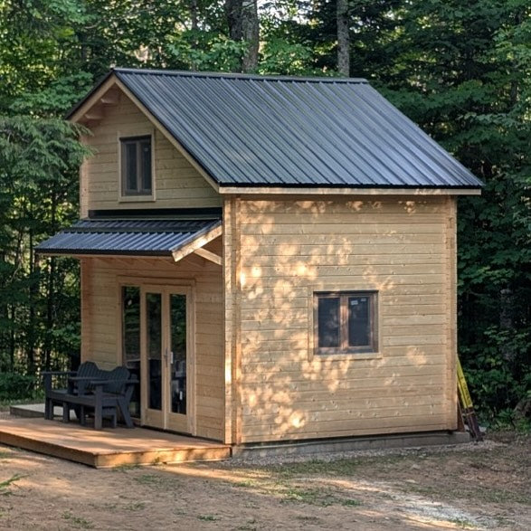 Small wooden cabin in a forest setting with a metal roof.