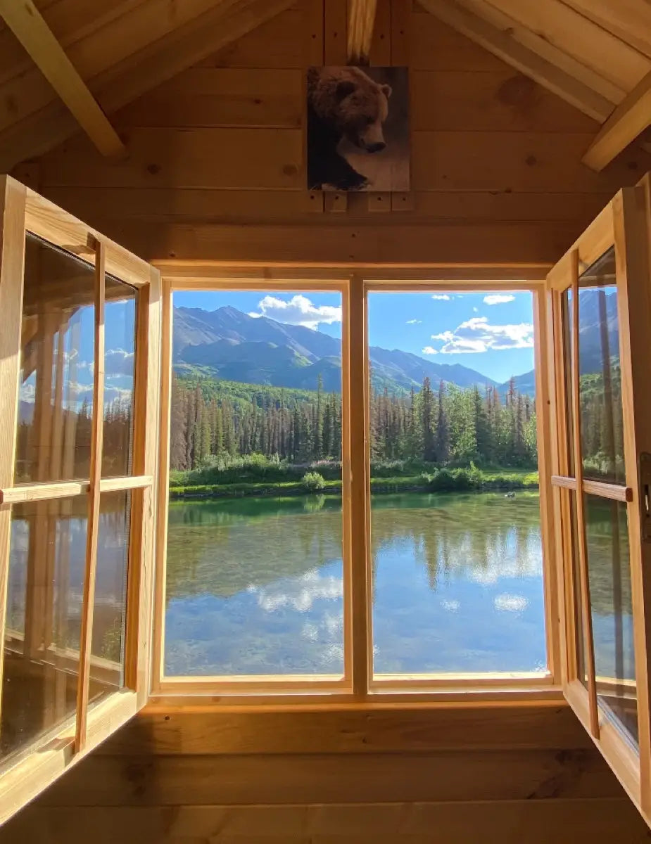 View from a wooden cabin with large windows overlooking a lake and mountains.