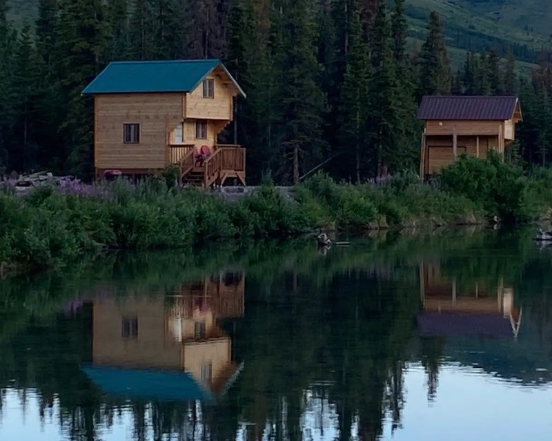 Two wooden cabins by a lake with trees in the background