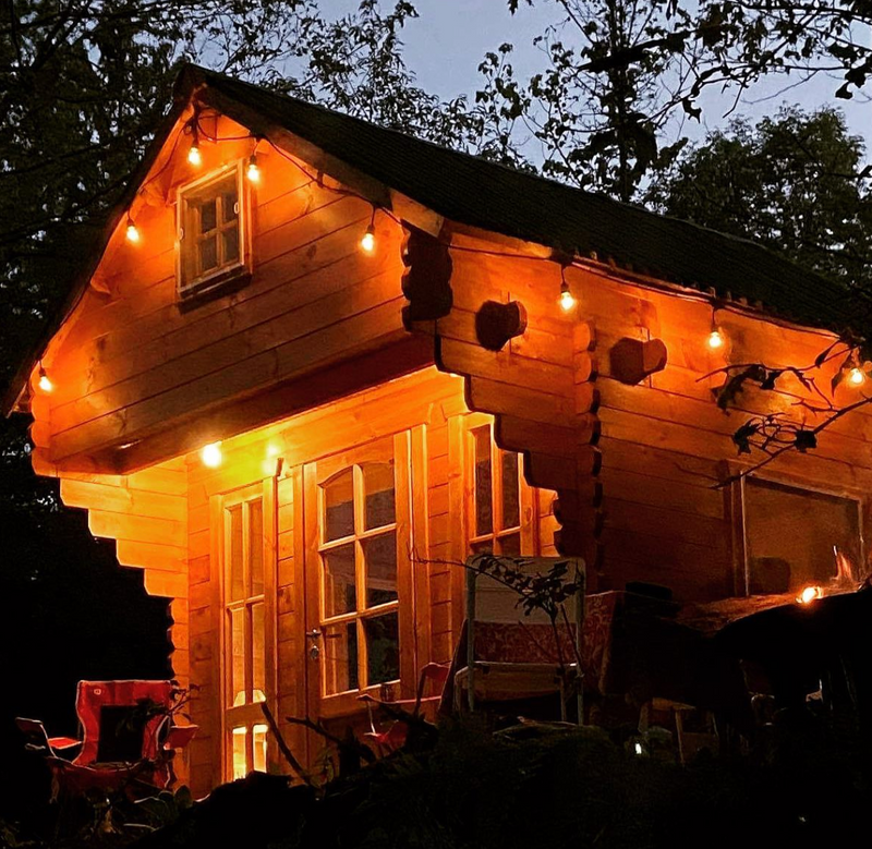 Wooden bunkie at night with string lights and outdoor furniture.
