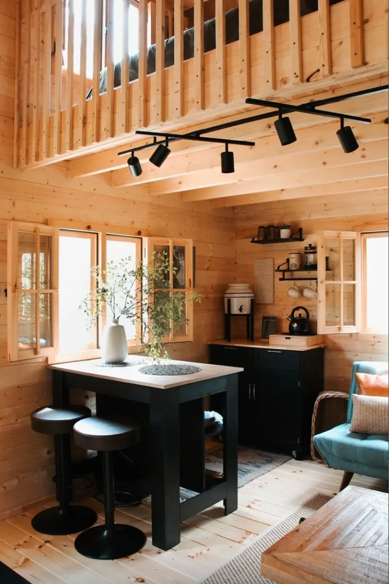 Modern kitchen inside a DIY cabin with wooden interior, black island, and stools.