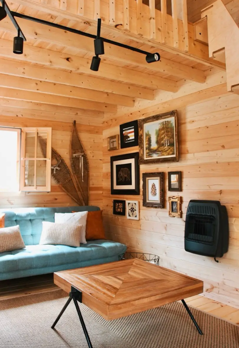 Wooden interior of a cabin with a blue sofa, wooden table, and framed pictures on the wall.